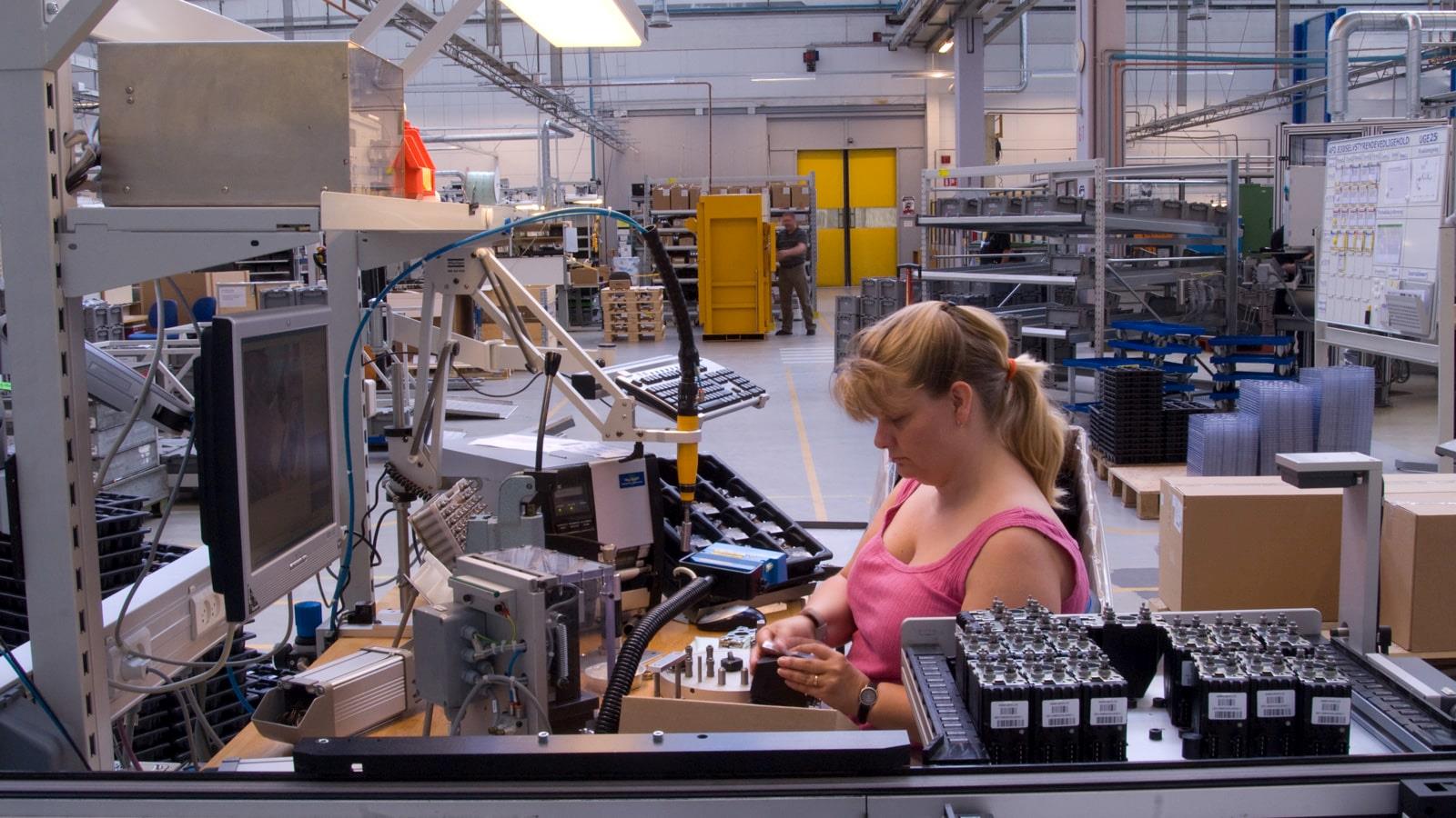 Blond woman in pink blouse working at assembly line at Sauer-Danfoss